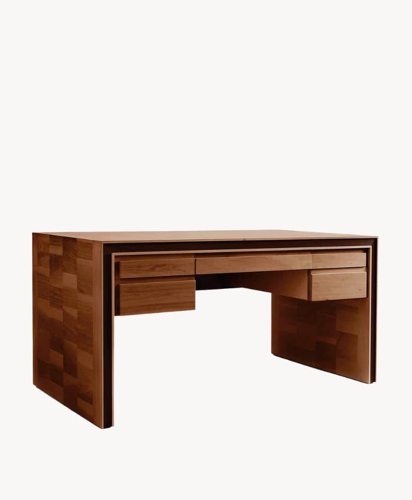 A modern wooden desk with a smooth finish, featuring three drawers—two smaller ones on the right and left and a larger center drawer. The desk has a minimalist, boxy design with visible wood grain patterns.