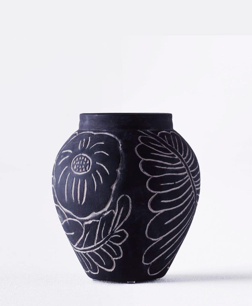 A black ceramic vase with white floral and leaf patterns etched into its surface, set against a plain white background.
