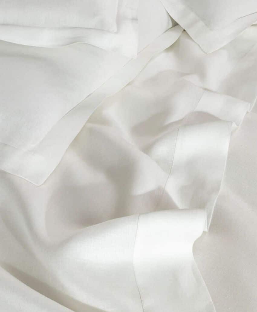 Close-up of white, rumpled bed sheets and pillowcases, showing smooth and soft fabric with natural folds and creases.