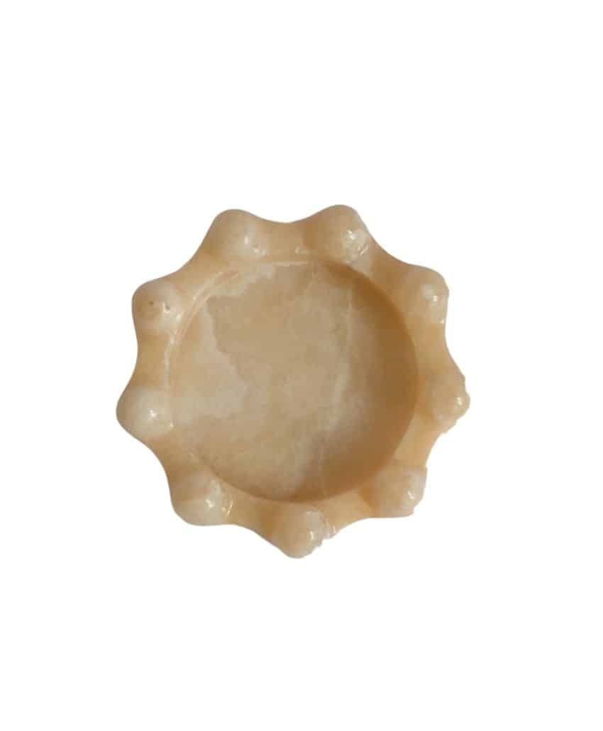 A round, light beige wax massage bar with a scalloped, bumpy edge, photographed on a white background.