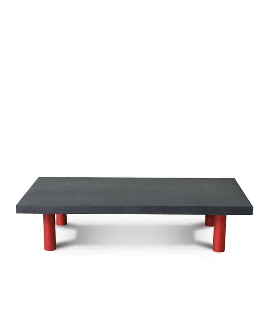 A minimalist, rectangular black table with four short, cylindrical red legs, set against a plain white background.