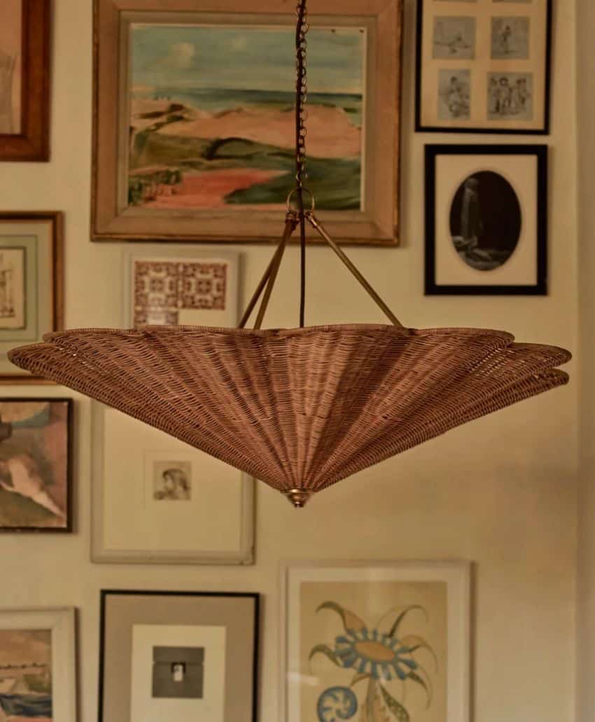 A woven rattan pendant light hangs from the ceiling in front of a wall decorated with various framed paintings, drawings, and photographs in different sizes and styles.
