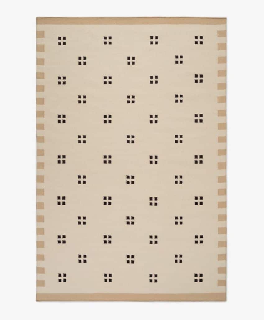 A rectangular beige rug with evenly spaced small black square clusters, each cluster made up of four small black squares. The rug has simple tan borders on the shorter sides.