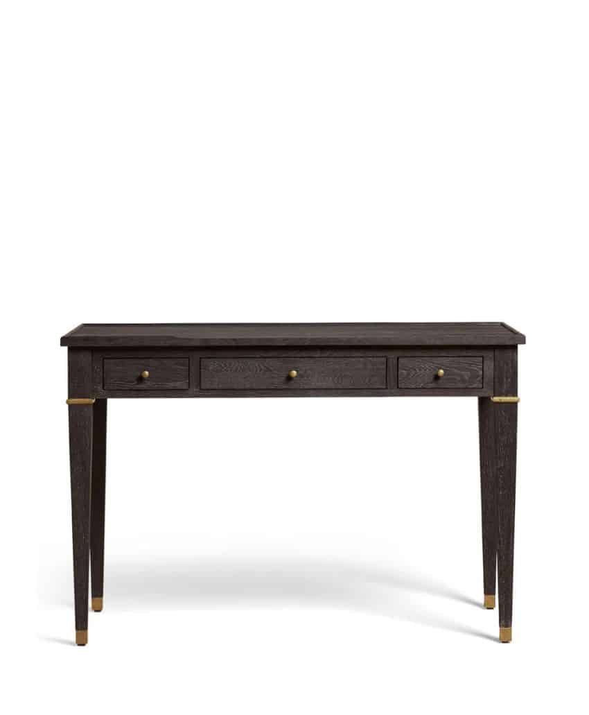A dark wooden desk with three front drawers, gold drawer knobs, and gold accents on the corners and feet, set against a white background.