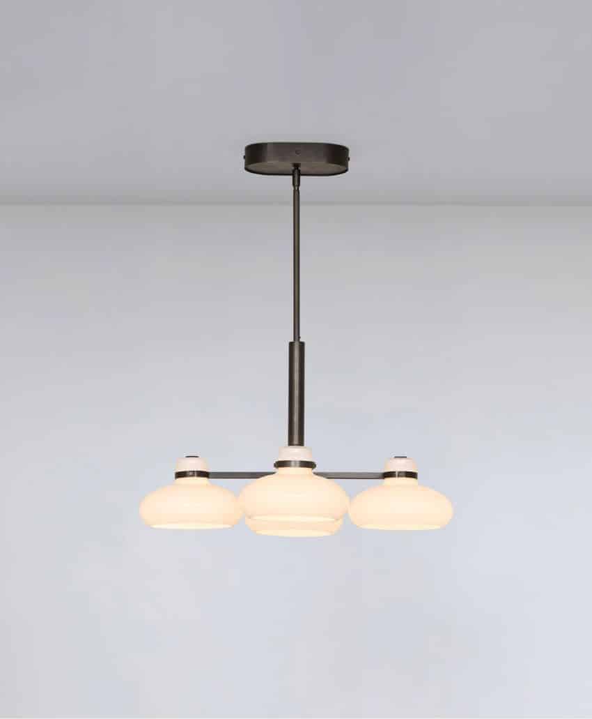 A modern ceiling light fixture with three round, frosted glass shades arranged in a row, supported by a dark metal frame and rod, against a plain light-colored ceiling.