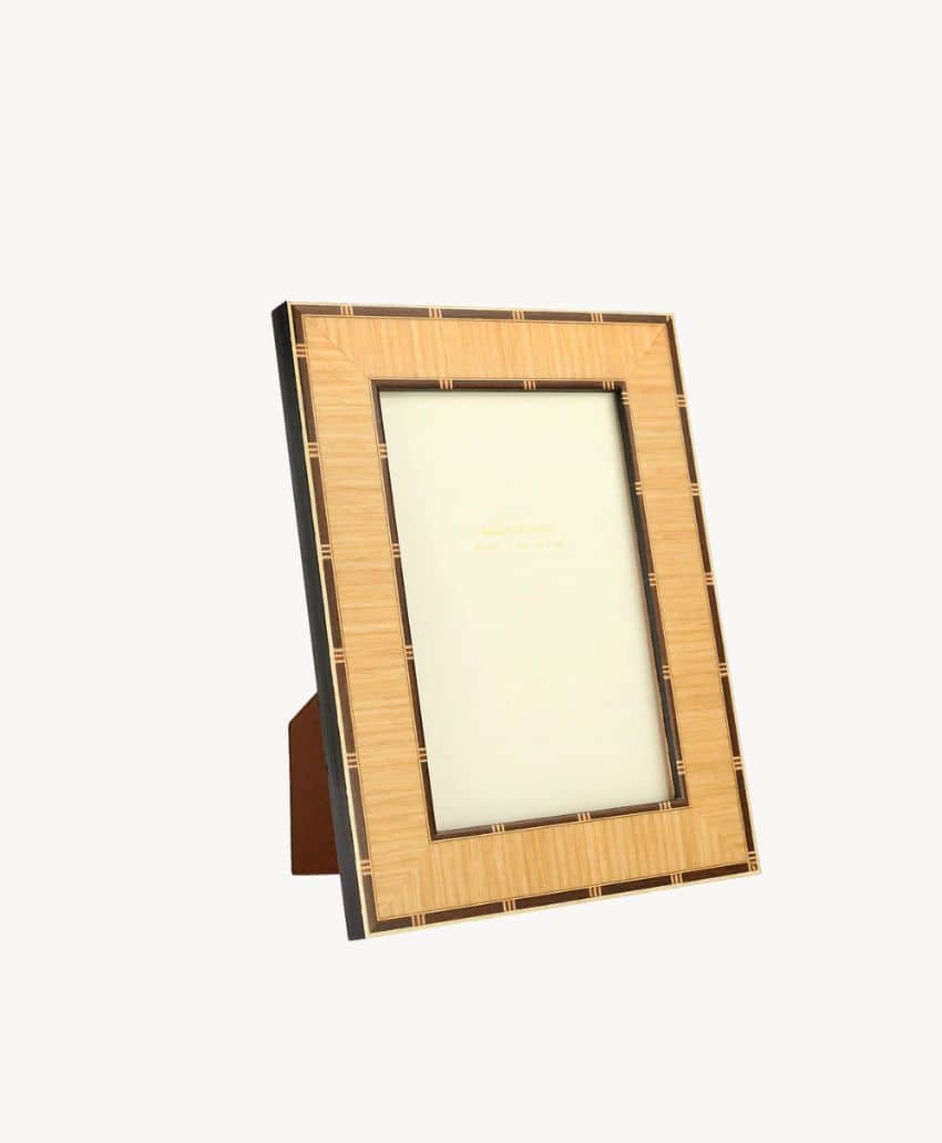 A wooden picture frame with a woven pattern stands upright on a plain white background, supported by an attached stand. The frame is empty, displaying a blank, light-colored insert.