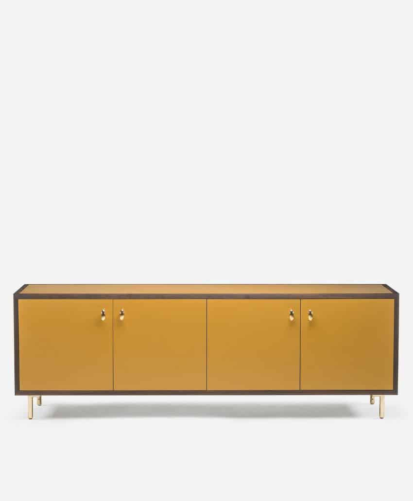 A modern, low-profile sideboard with a mustard yellow front, four cabinet doors, small gold handles, and gold legs, set against a plain white background.