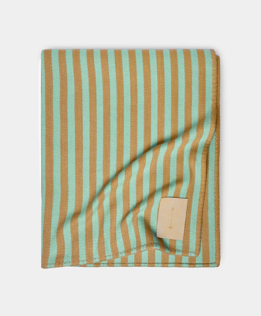 A neatly folded blanket featuring alternating vertical stripes in light teal and tan colors, with a small beige fabric tag sewn onto one corner.