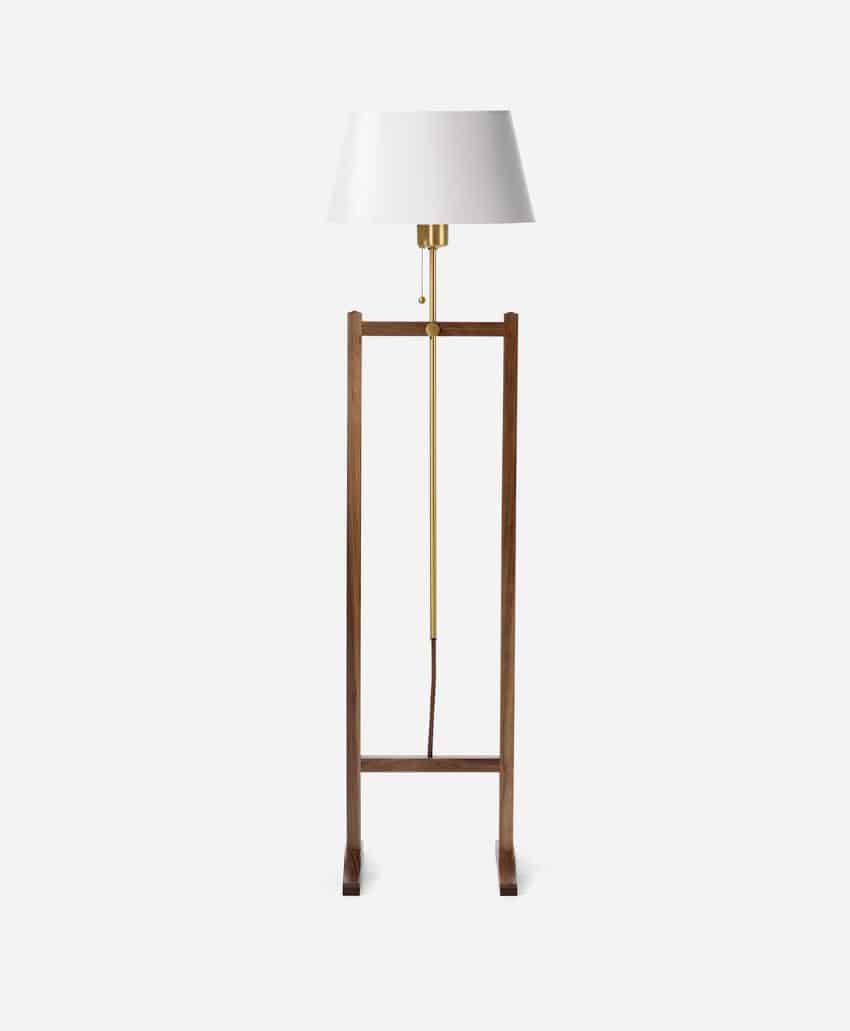 A modern floor lamp with a white lampshade, brass stand, and wooden rectangular base, set against a plain white background.