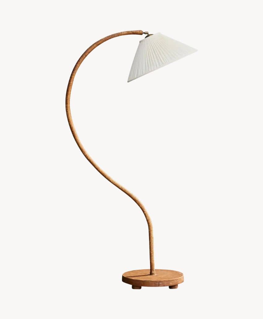 A modern floor lamp with a curved, woven stem, a round wooden base, and a white pleated lampshade, set against a plain, light background.
