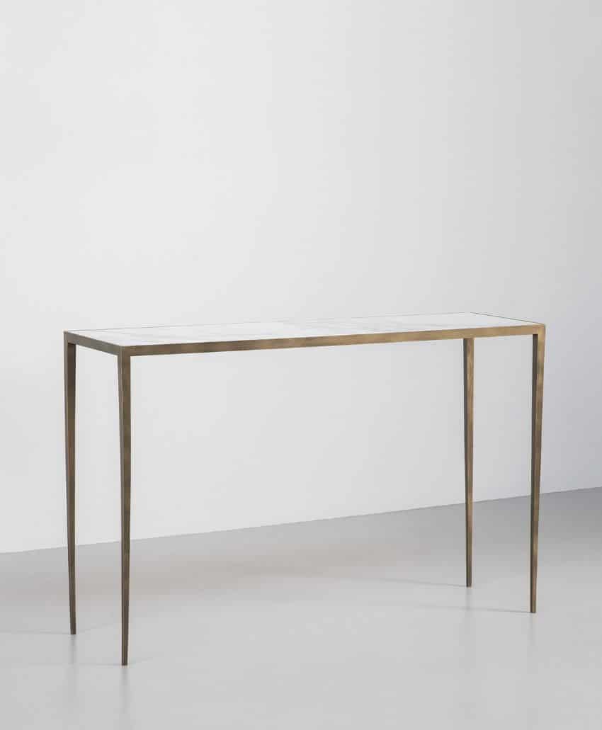 A minimalist console table with a thin, rectangular white top and slender metallic legs, placed against a plain white wall on a light gray floor.