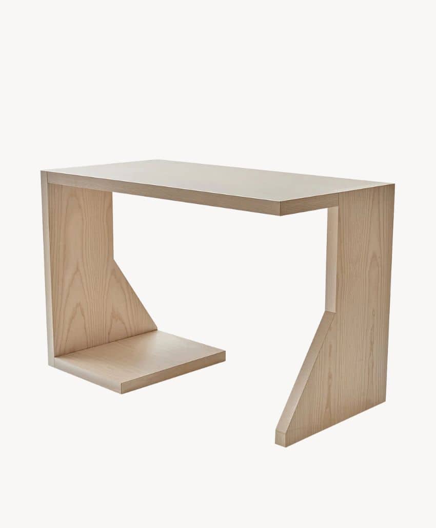A modern wooden desk with a light wood finish, featuring an asymmetrical design with one angled support and one rectangular support. The desk has clean, minimalist lines and an open base.