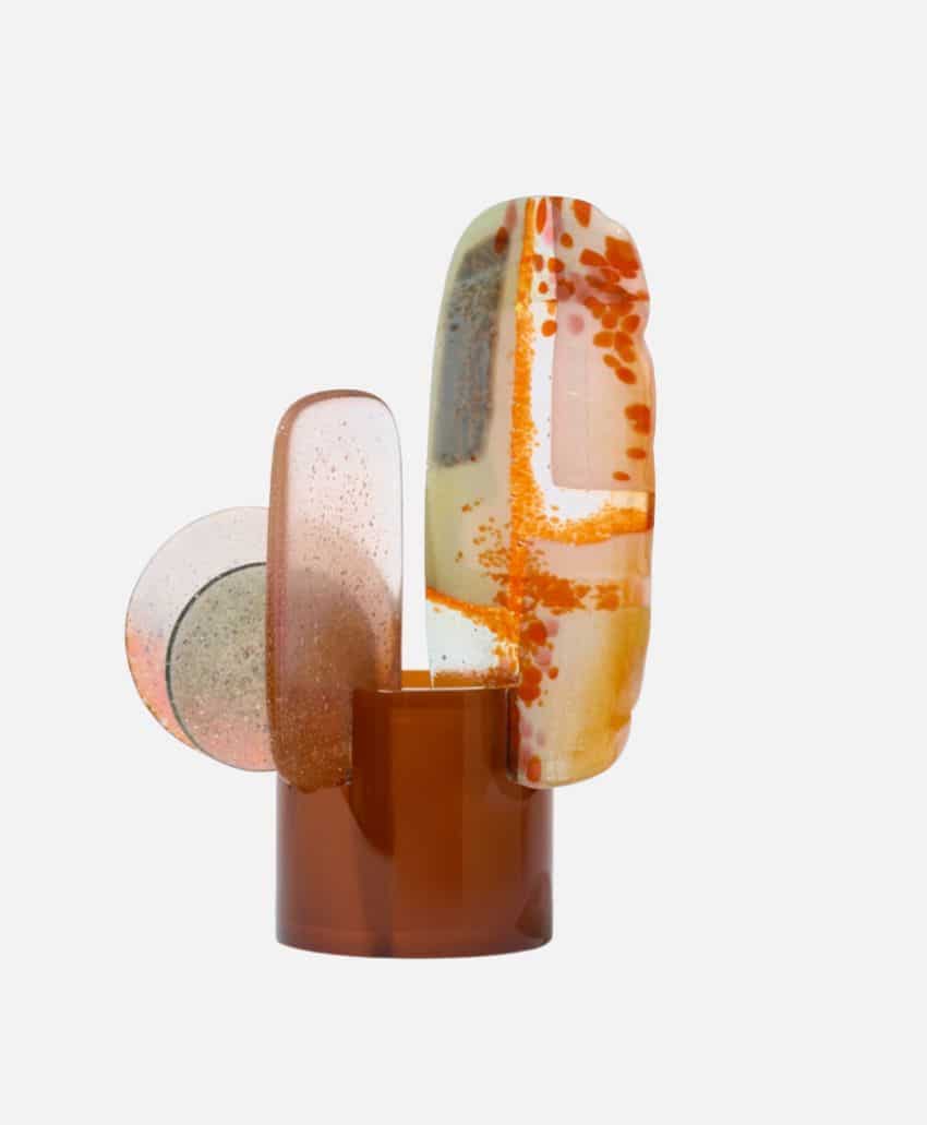 A modern abstract sculpture with translucent, overlapping shapes in brown, beige, and orange hues, arranged vertically on a brown circular base.