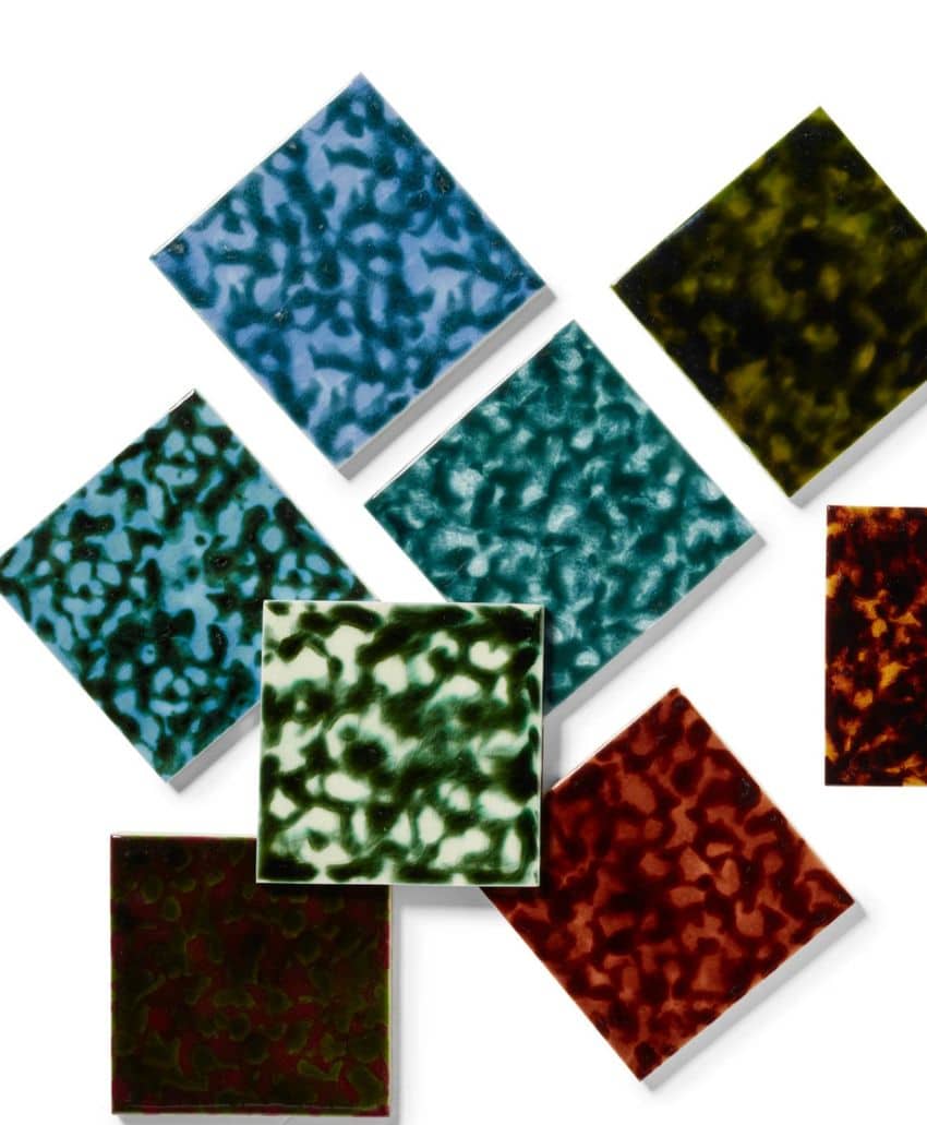 Eight square ceramic tiles with speckled, marbled patterns in blue, green, teal, black, and reddish-brown colors, arranged in a scattered overlapping layout on a white background.