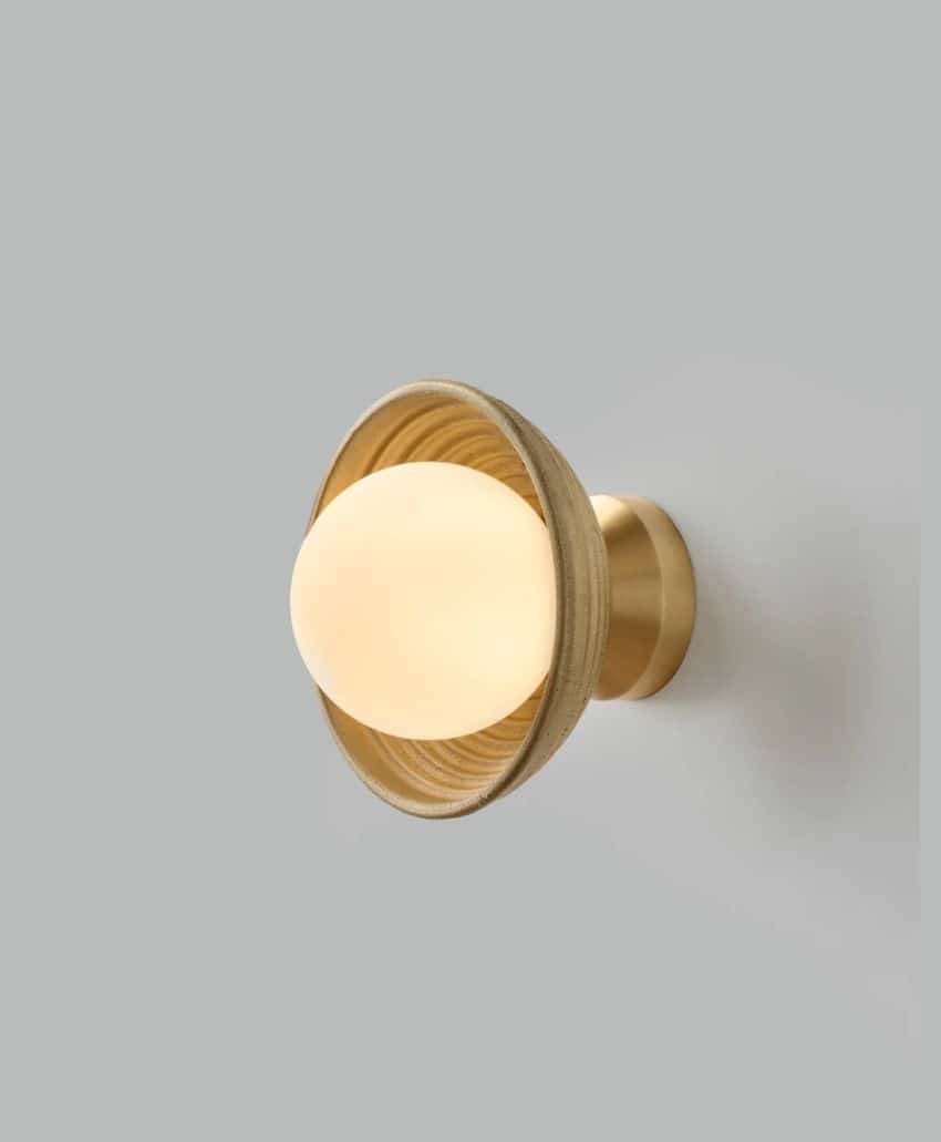 A modern wall sconce with a round frosted glass shade, surrounded by a circular wooden frame and mounted on a brass fixture, against a plain light gray background.