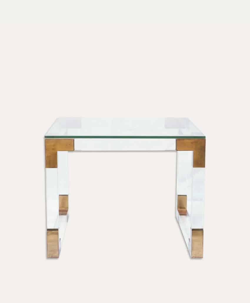 A clear acrylic side table with a glass top and gold metal corner accents, set against a plain white background.