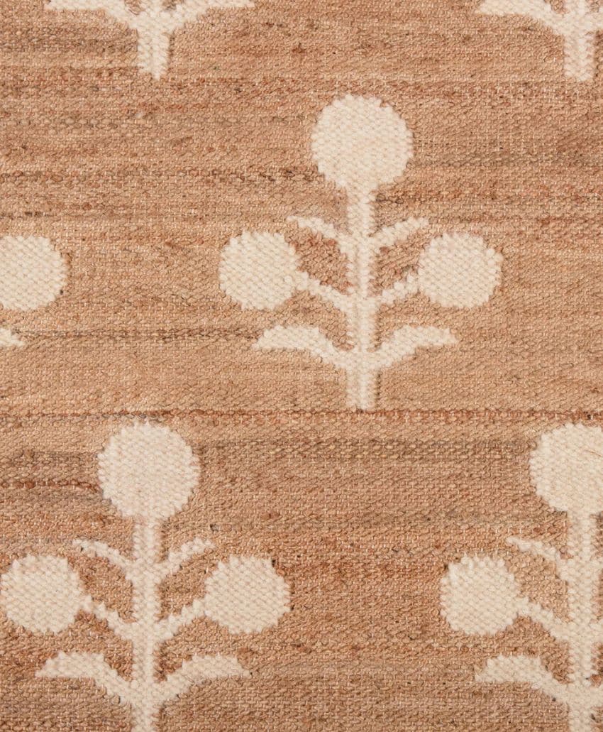 Brown textured fabric with a repeating pattern of simple white floral motifs, each consisting of three circular flower shapes connected by stems and leaves. The design is evenly spaced and symmetric.