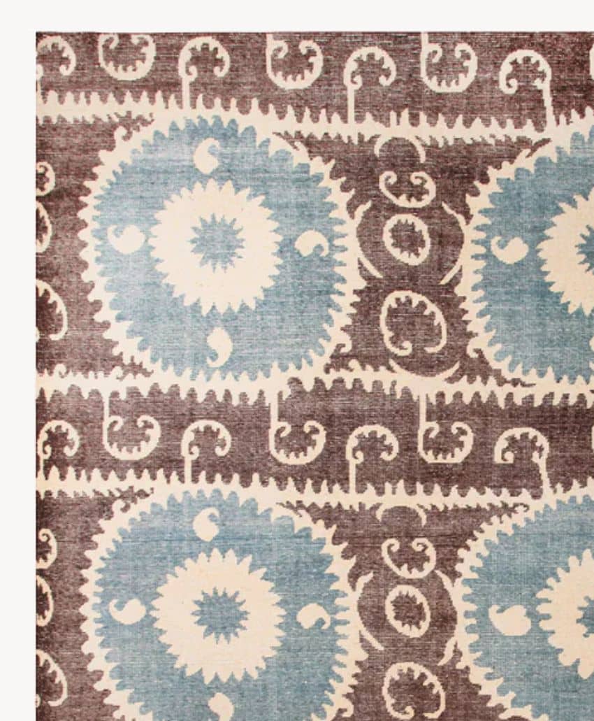 A patterned rug featuring large blue circular medallions with jagged edges, arranged in rows, interspersed with brown, swirling paisley and vine motifs on a cream background.