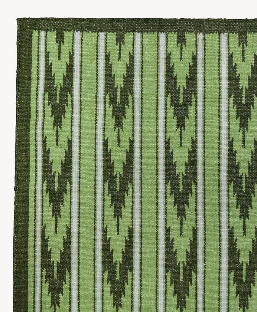 Close-up of a woven green mat featuring vertical stripes and arrowhead-like zigzag patterns in dark and light green tones, bordered by a solid dark green edge.