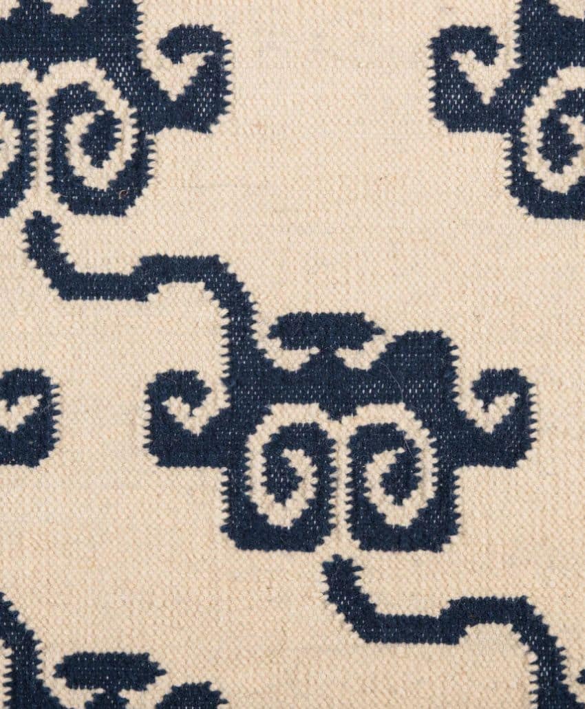 A beige fabric with a repeating pattern of abstract, dark blue swirling shapes that resemble stylized clouds or waves, woven with visible stitching.