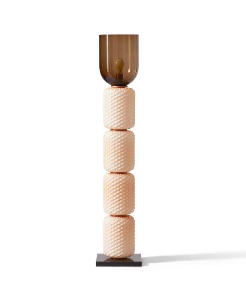 A modern floor lamp with a tall base made of four textured, cream-colored cylindrical blocks stacked vertically, topped with a translucent brown glass lampshade, standing on a square black base.