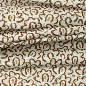 Beige fabric with a repeating, abstract brown floral pattern, shown in several folded layers. The texture of the material and the intricate design are clearly visible.