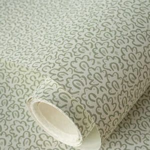 A roll of wallpaper with a repeating, abstract floral or paisley pattern in muted green on a light beige background. The wallpaper is partially unrolled, showing the design clearly.