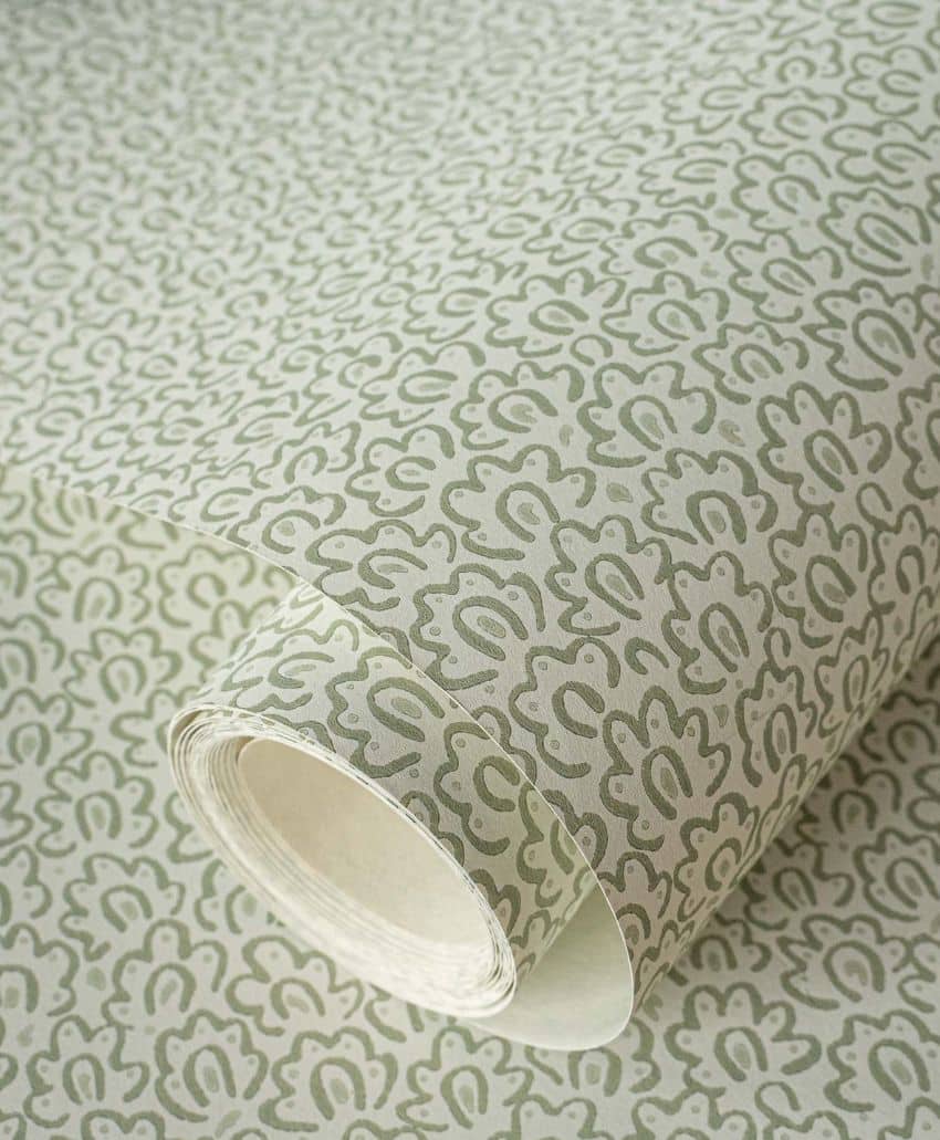 A roll of wallpaper with a repeating, abstract floral or paisley pattern in muted green on a light beige background. The wallpaper is partially unrolled, showing the design clearly.