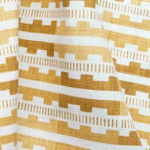 Close-up of yellow and white woven fabric with a geometric pattern featuring horizontal stripes and stepped shapes. The fabric is slightly wrinkled, showing its texture and flexible nature.