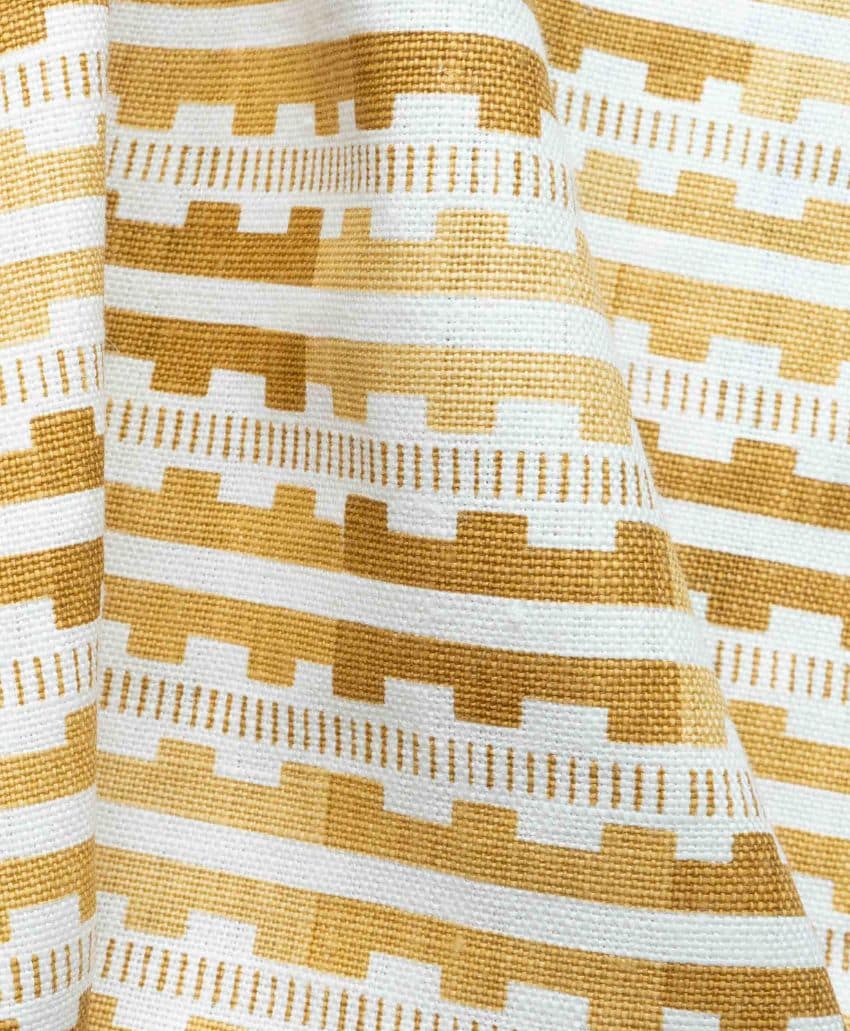 Close-up of yellow and white woven fabric with a geometric pattern featuring horizontal stripes and stepped shapes. The fabric is slightly wrinkled, showing its texture and flexible nature.