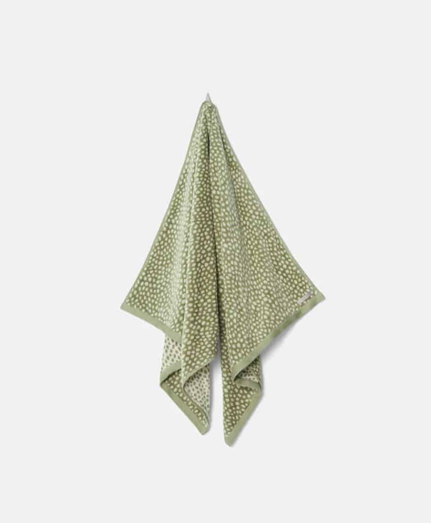 A green towel with a light-colored dotted pattern hangs on a wall against a plain, light background.