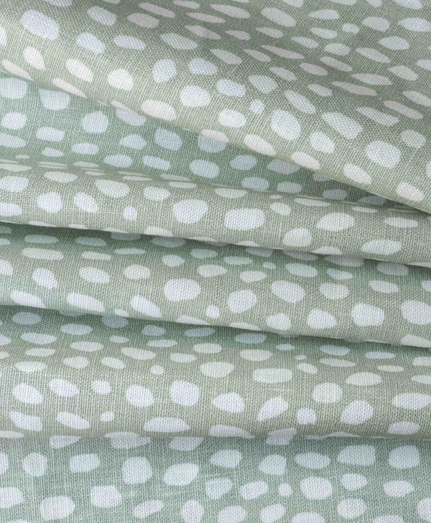 Stacked layers of pale green fabric with an irregular white dot pattern, creating a soft, textured appearance.