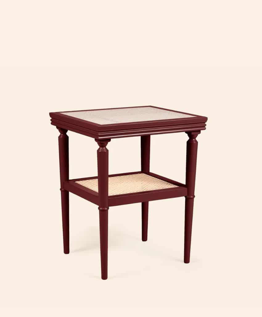 A wooden side table with a dark red frame, four tapered legs, and two cane shelves, set against a plain beige background.