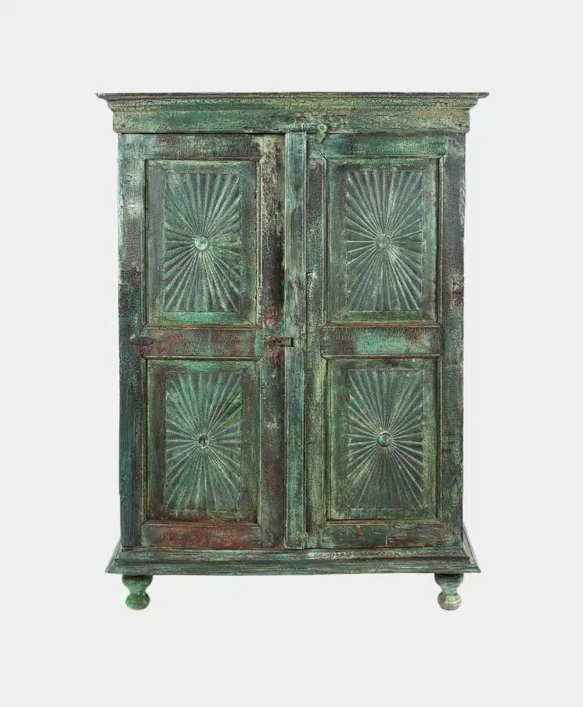 A vintage wooden cabinet with a distressed green finish, featuring two doors with carved sunburst patterns and standing on four short legs.