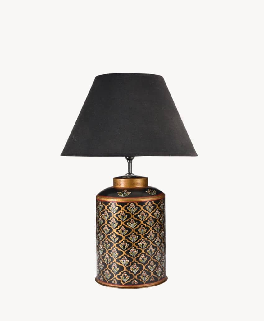 A decorative table lamp with a black, gold-patterned cylindrical base and a plain black lampshade, set against a white background.
