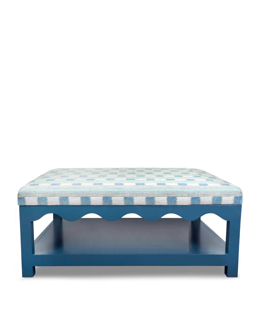 A blue wooden ottoman with a lower shelf and a cushioned seat featuring a light blue and white checkered pattern. The frame has a decorative scalloped edge.