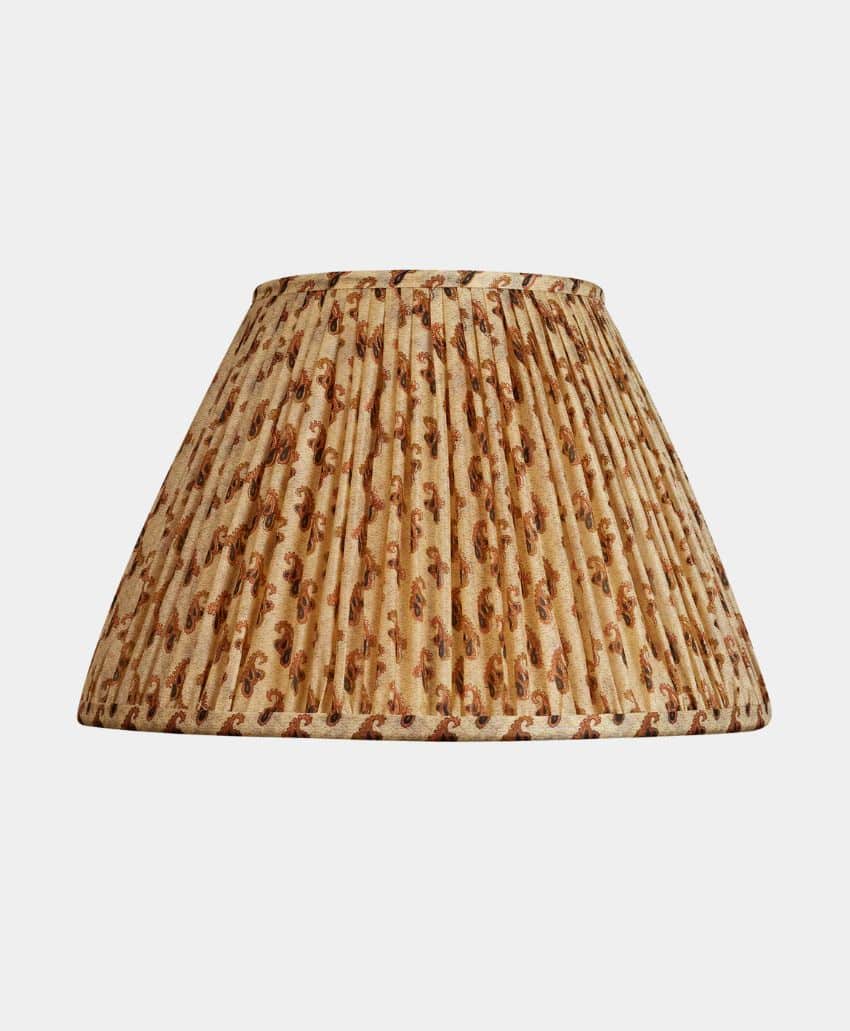 A pleated fabric lampshade with a beige background and a brown floral or leaf pattern, set against a plain white backdrop.