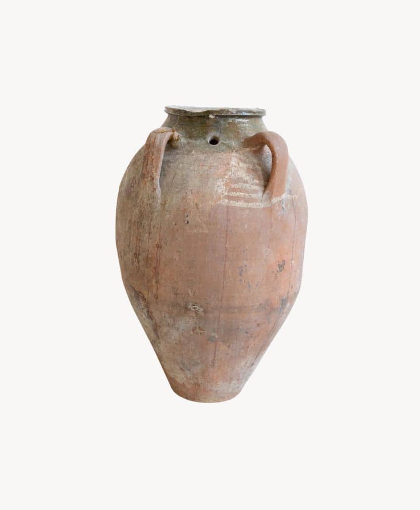 A large, weathered clay amphora with two handles and a narrow neck, showing signs of age and patina, set against a plain white background.