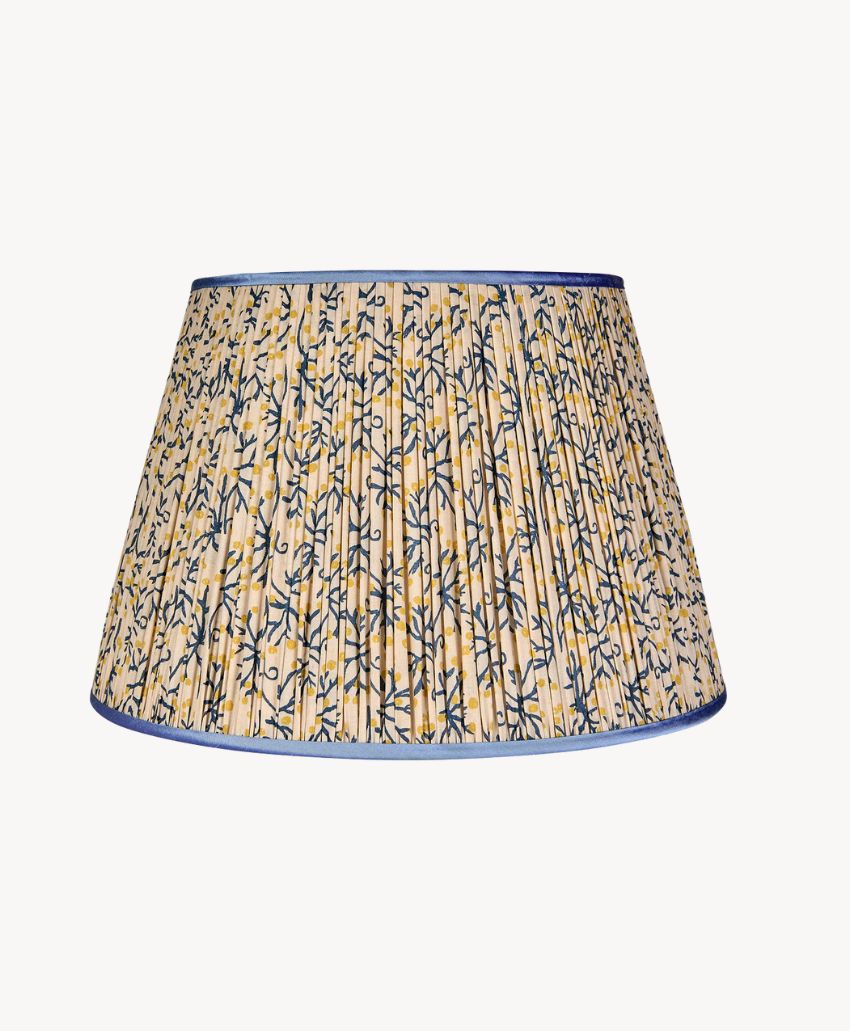 A pleated fabric lampshade with a blue and yellow floral vine pattern on a cream background, finished with blue trim at the top and bottom edges.