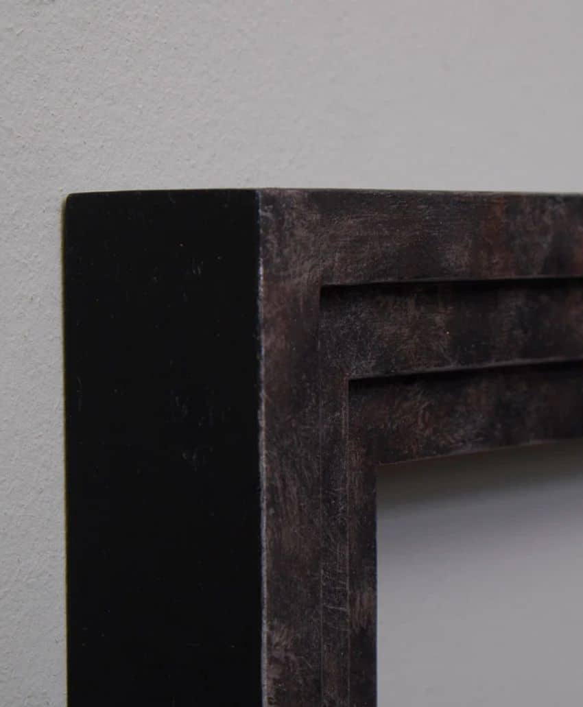 Close-up of the upper corner of a dark, rectangular picture frame mounted on a light-colored wall, showing its texture and minimalist, modern design.