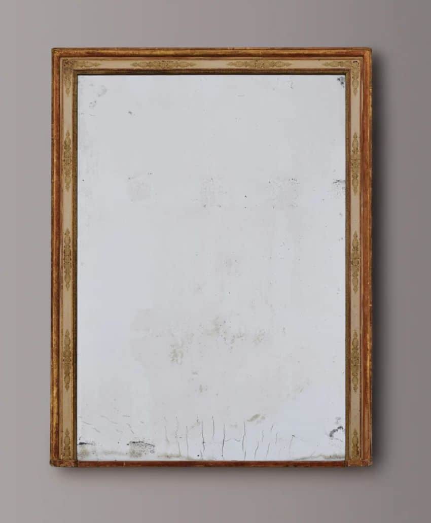 An empty, worn-out picture frame with a gold and brown border hangs on a plain gray wall. The frame contains a blank, slightly stained and cracked white canvas.