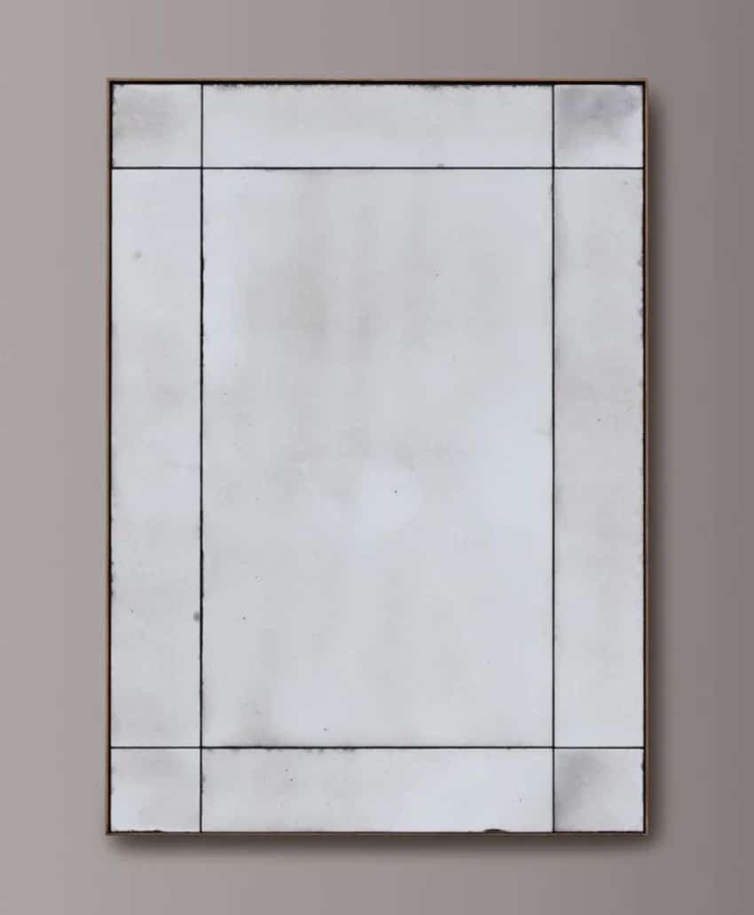 A rectangular, distressed mirror with a minimalistic grid design and visible lines dividing the edges, mounted on a plain gray wall.