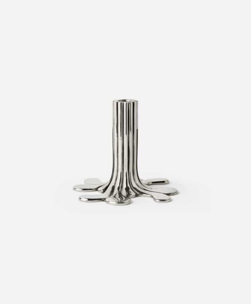 A silver, metallic candle holder with a unique, organic design resembling melted metal or dripping liquid, standing upright on a plain white background.