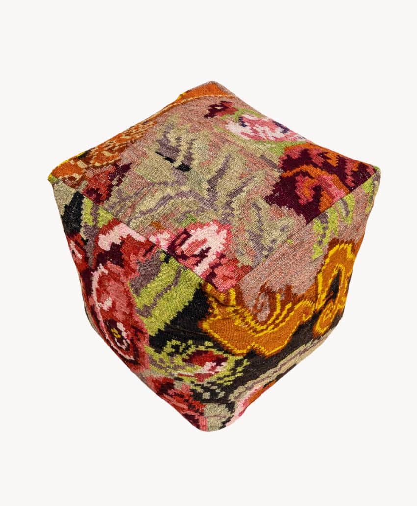 A fabric-covered cube pouf with a colorful floral pattern in shades of red, pink, yellow, green, and orange on a light background, viewed at an angle against a plain white backdrop.