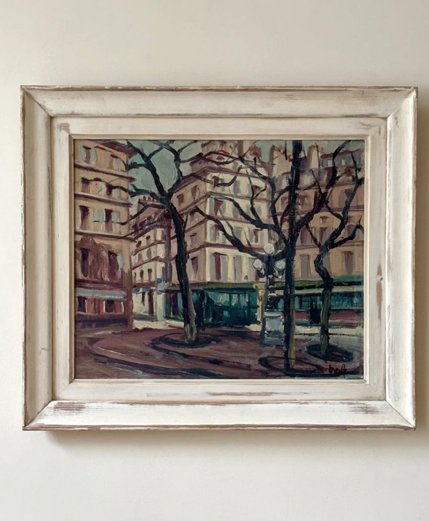 A framed painting of a city street with bare trees, buildings with many windows, and a curved road. The scene has muted colors and an impressionistic style, giving a vintage, urban atmosphere.