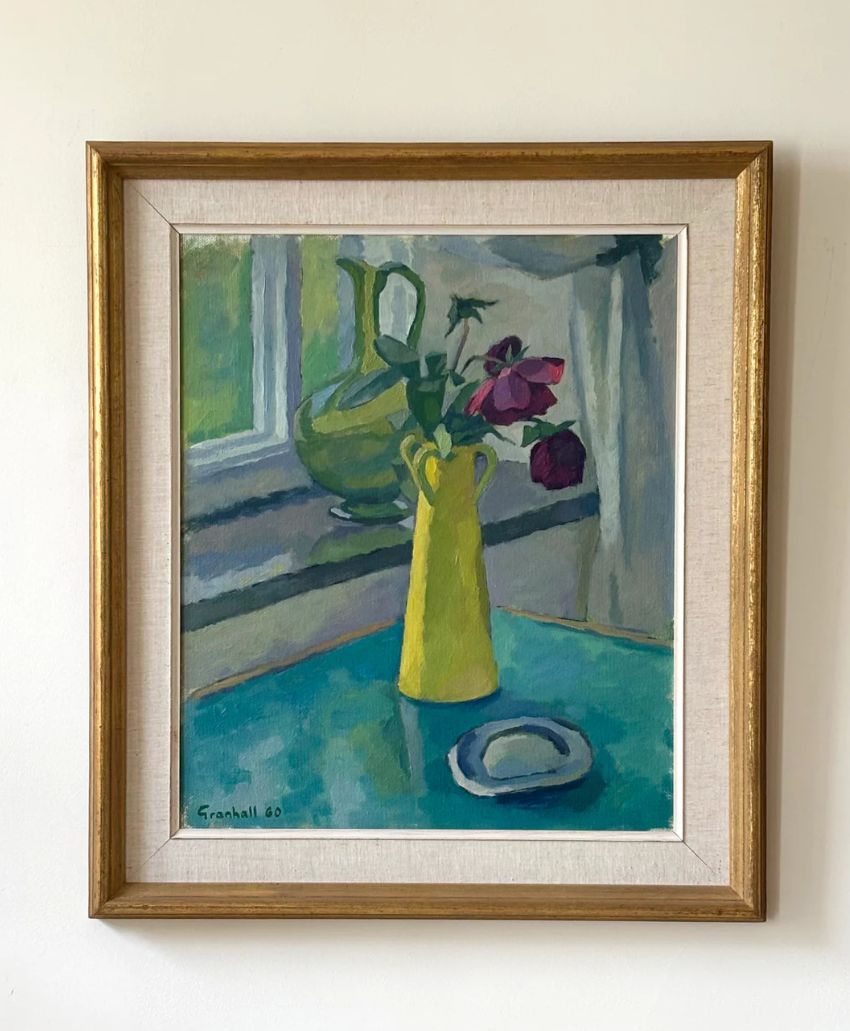 A framed painting shows a yellow vase with red flowers on a blue-green table by a window. A green jug and more flowers are in the background. The painting is signed Granhall 80 in the bottom left corner.