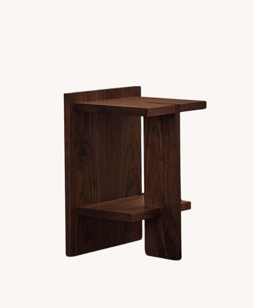 A modern, minimalist wooden side table with two staggered shelves and a dark wood finish, set against a plain white background.