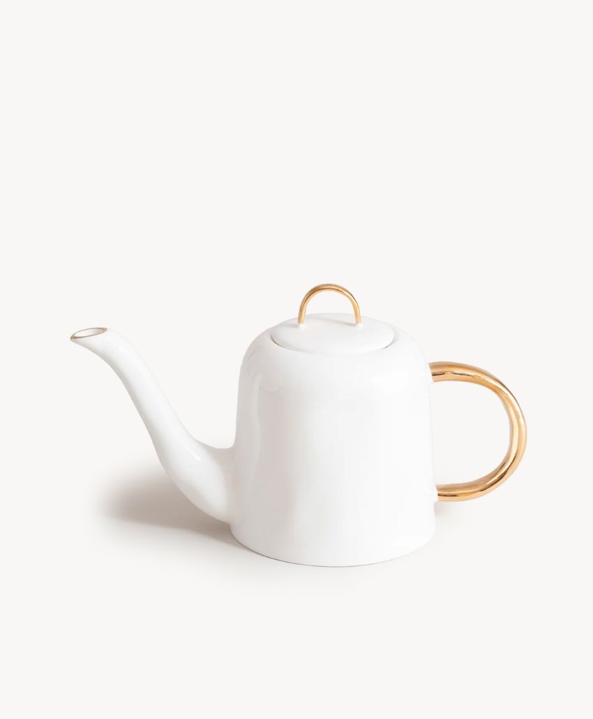 A white ceramic teapot with a curved spout, a rounded body, and gold accents on the handle and lid, set against a plain light background.