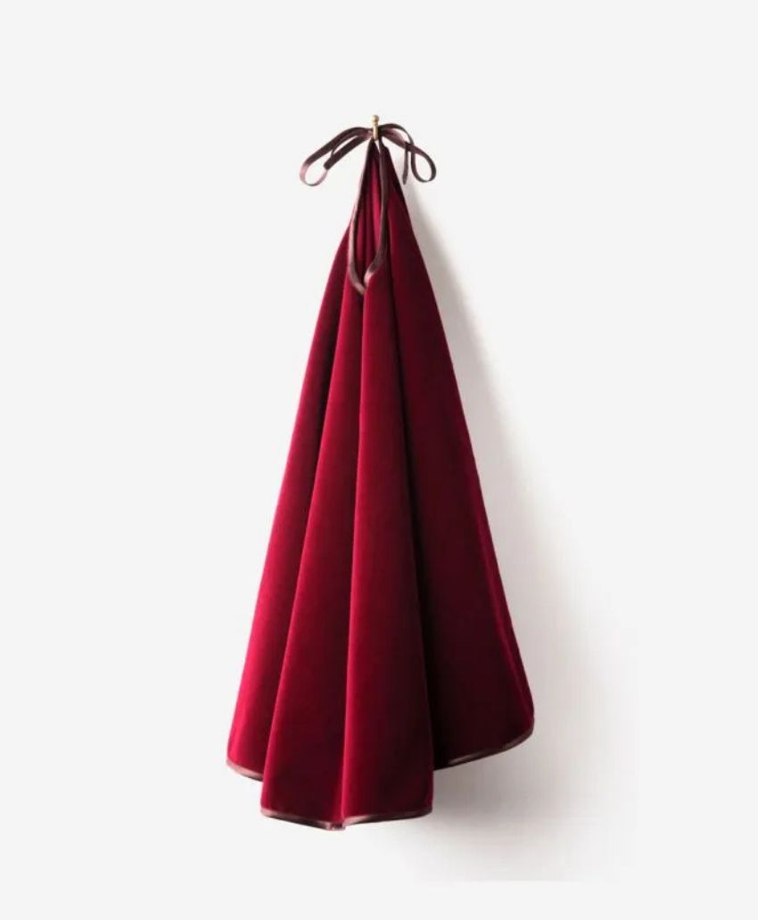 A deep red velvet cloth hangs neatly from a hook by a matching tied ribbon, draping in soft folds against a plain white background.