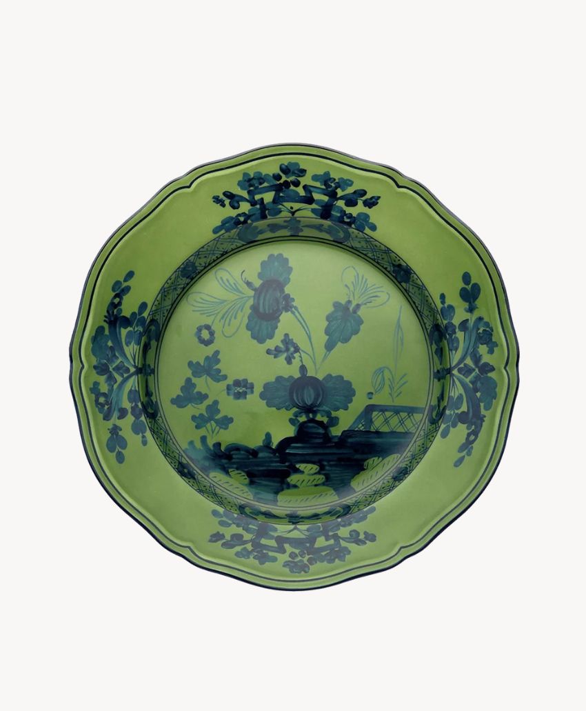 A decorative green porcelain plate with blue floral patterns and a scenic design, including trees and a bridge, around the center and along the scalloped rim.